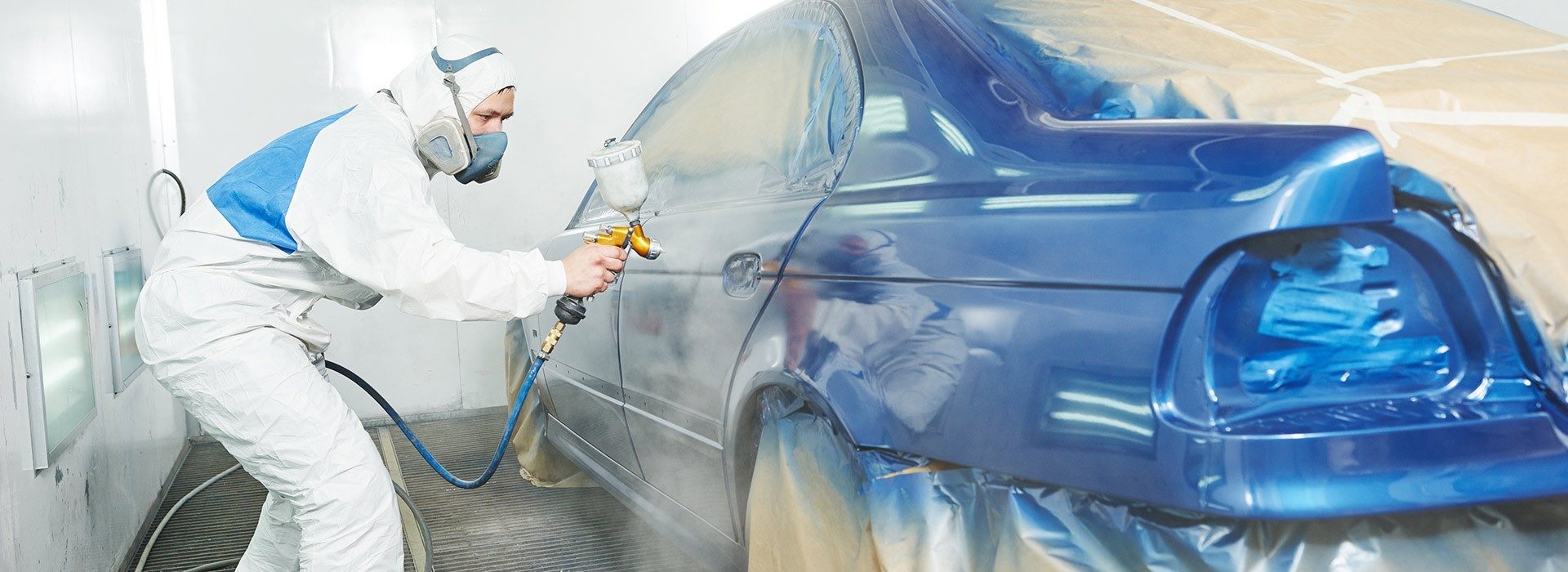Lackierer der Stiller GmbH lackiert eine Fahrzeugtür in blauem Metallic-Lack in der Lackierkabine